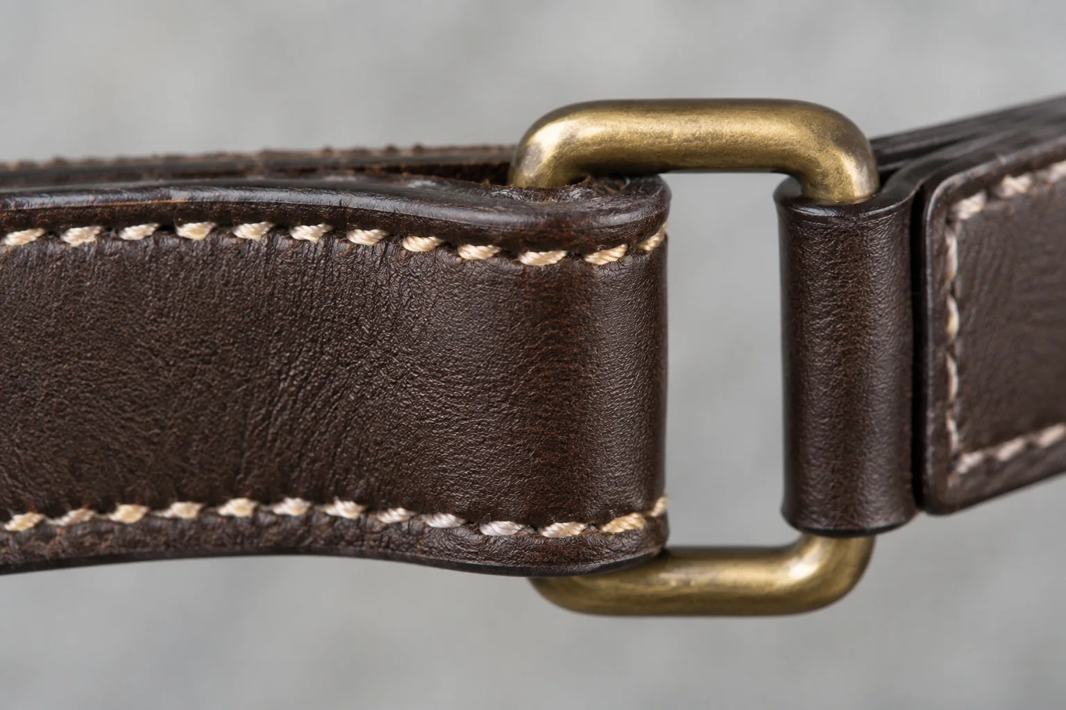 Dettaglio illustrativo di cuciture, bordi rifiniti e anello in ottone di un cinturino in pelle